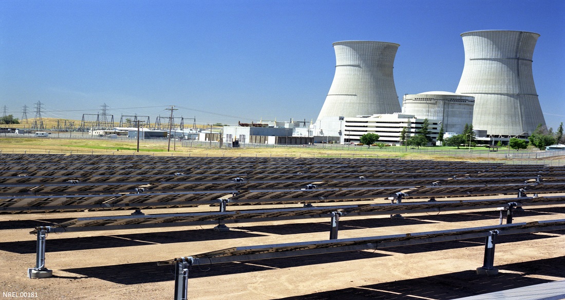 a field of solar panels with a pair of cooling towers in the background