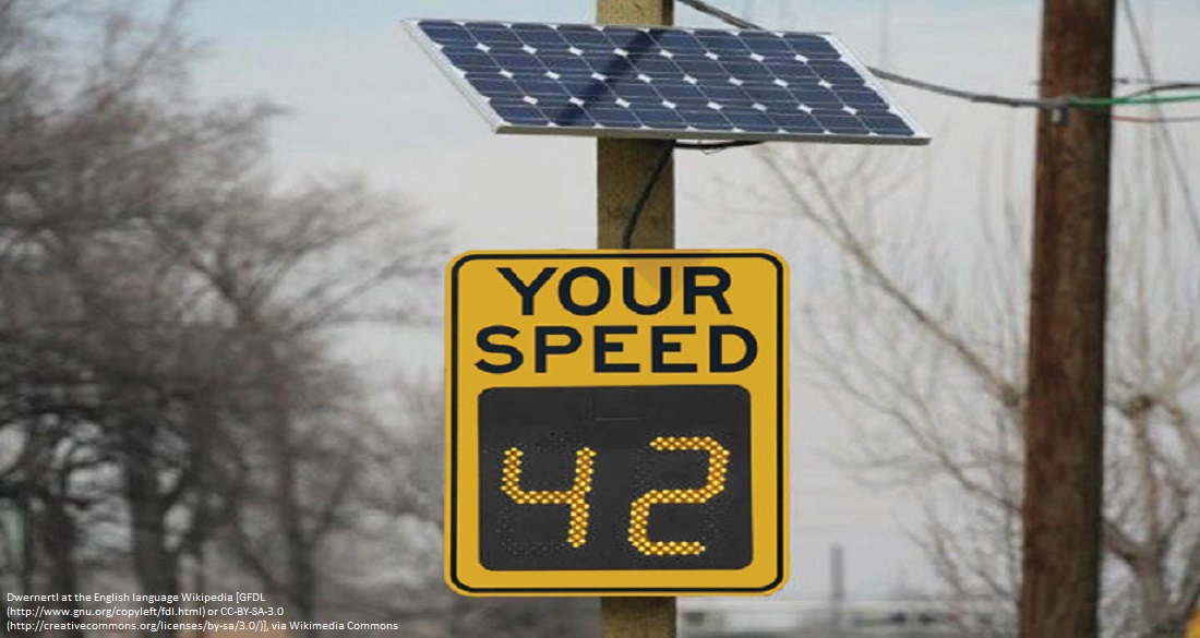 A digital sign equipped with a radar used to measure and display the speed of traffic is powered by a solar panel mounted above it.